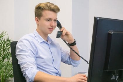Mann (AdWords Trainer) mit Telefonhörer in der Hand, schaut auf Monitor